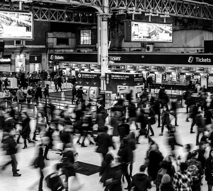 Dynamic black and white image capturing a busy train station with a crowd of commuters.